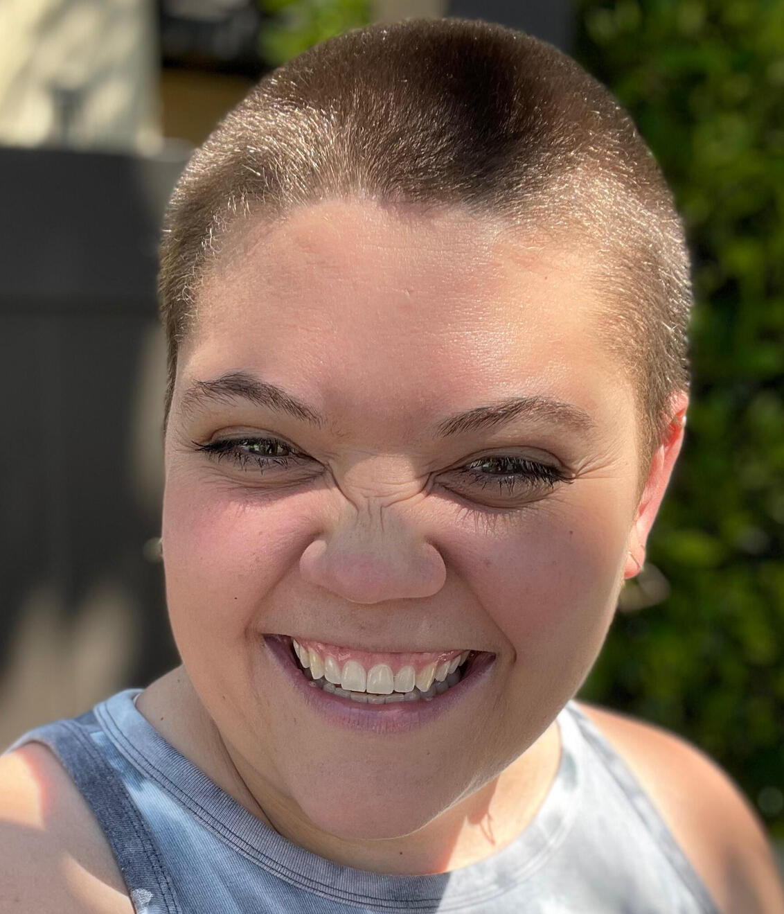 Evan Chelsee This is a picture of Evan smiling. Their nosed is scrunched up in a way that's pretty cute. They have a buzzcut too.